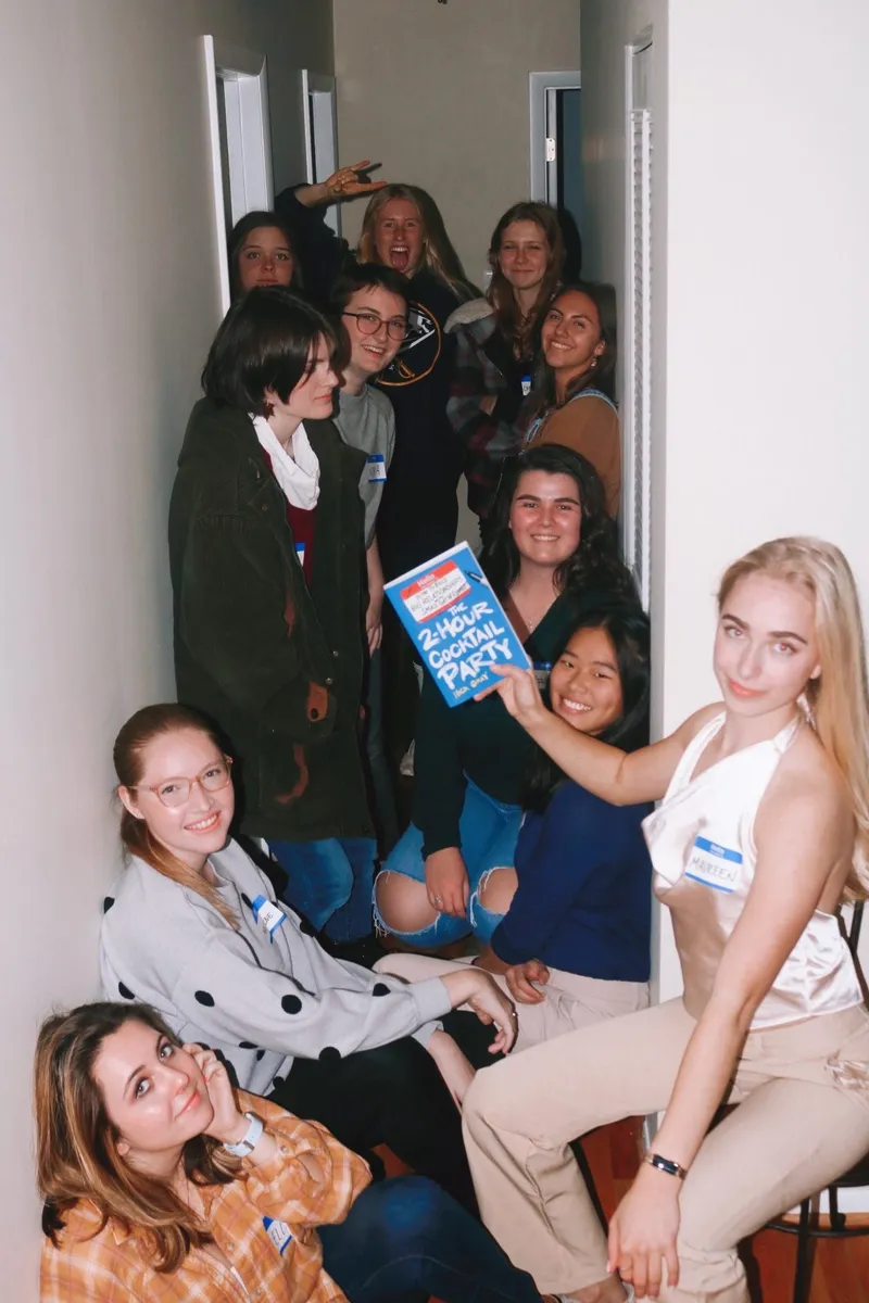 group of people in the hallway sitting and standing, smiling, one holding 'The 2-Hour Cocktail Party' book