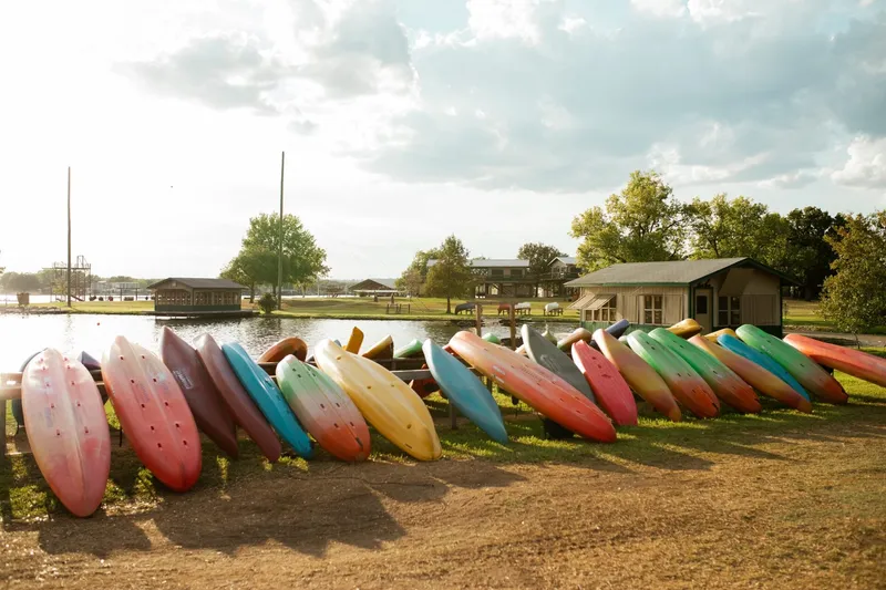 a bunch of canoe lined up on a ground with grass beside a body of water