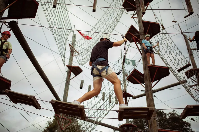 3 people with helmets and rappelling ropes walking on a wood bridge