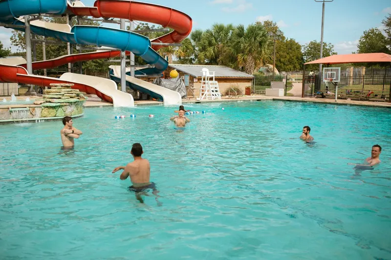 Men swimming in outdoor pool with slides in adult summer camp