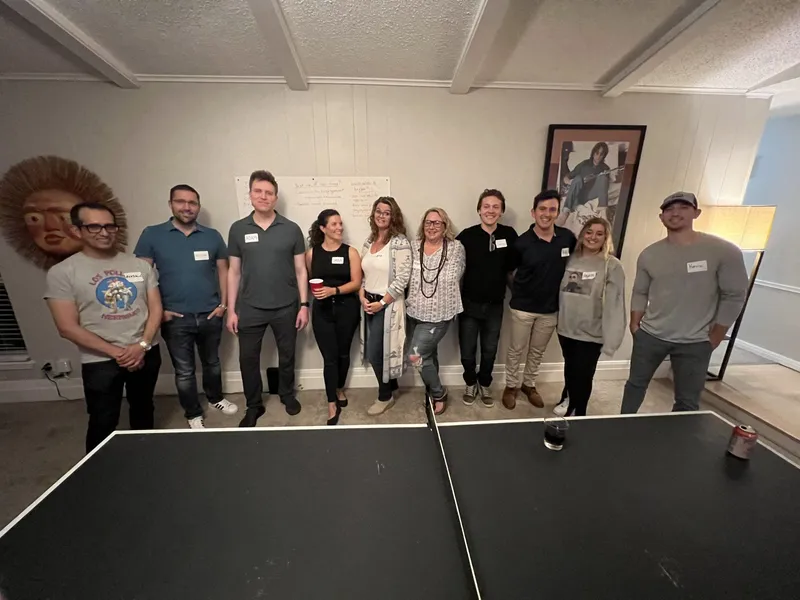 group of people with name tags smiling an a ping pong table at the front