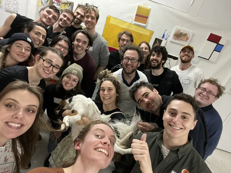 A group of people with name tags smiling indoors and a dog in the middle.