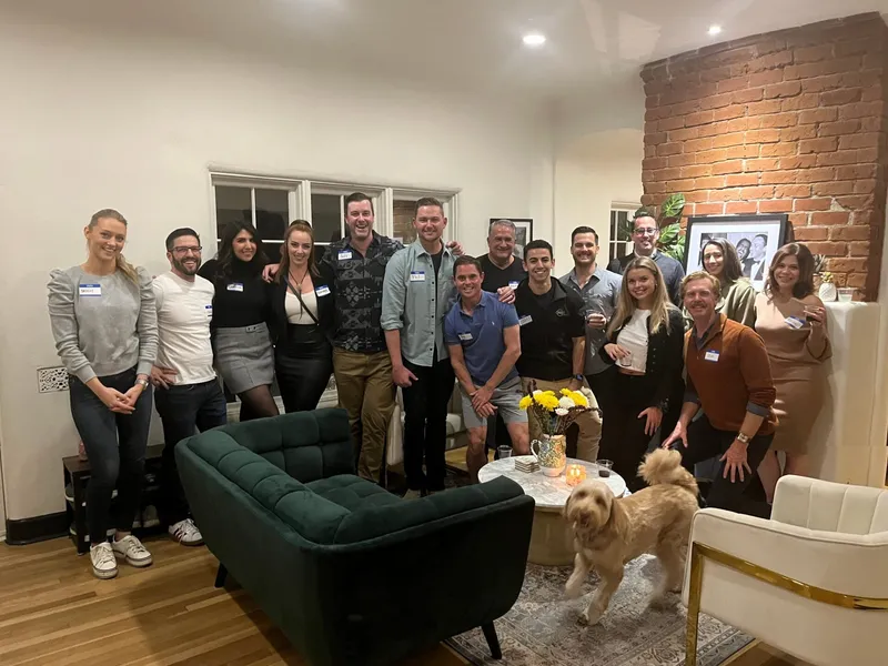 A group of people with name tags smiling indoors, with a green couch, and a dog at the bottom-right.