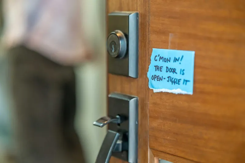 photo of a door zoomed in on the doorknob with a ripped blue paper on it saying 'c'mon in! the door is open - jiggle it'