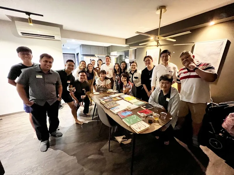 group of people with name tags smiling, surrounding a table full of books