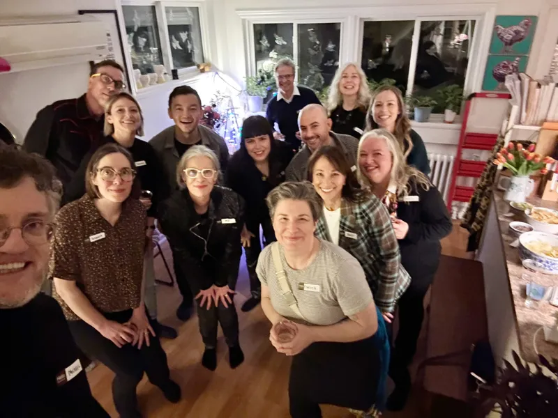 A group of people with name tags smiling, indoors, with party food on the right.